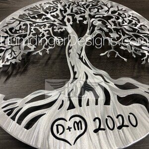 May include: A silver metal tree of life wall art with a heart-shaped design and the initials "D+M" and the year "2020" engraved below.