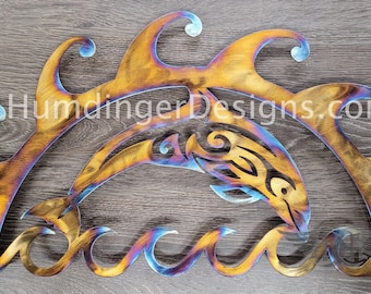 May include: A metal wall art sculpture of a dolphin jumping through waves. The dolphin is stylized with a tribal design and the waves are flowing and abstract. The metal has a rainbow iridescent finish.