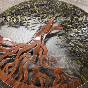 May include: A round metal wall art piece featuring a tree of life design. The tree is cut out of the metal and has a brown wood grain finish on the bottom half and a gold finish on the top half. The tree is surrounded by a circle of metal with a wood grain finish.