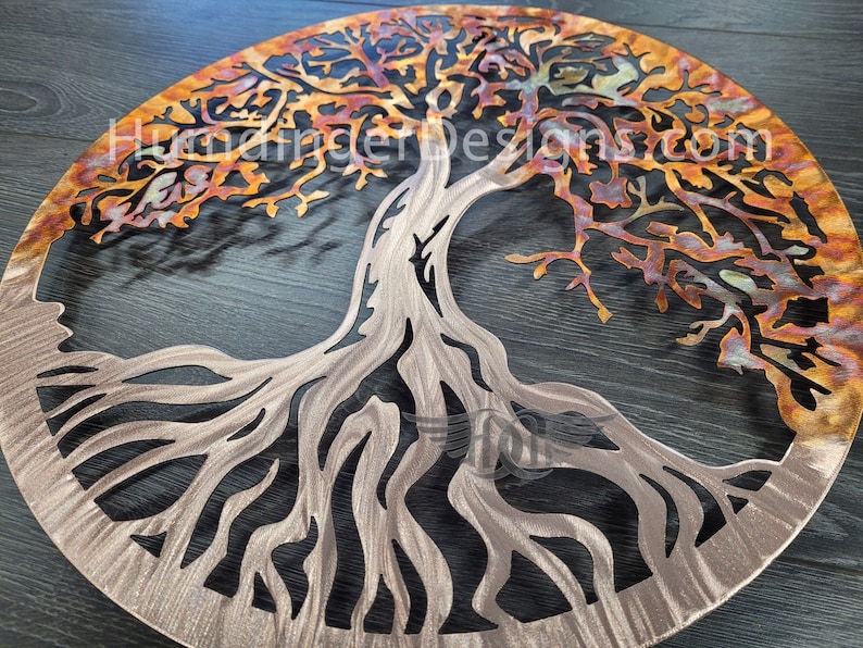K&ouml;nnte beinhalten: Eine runde Wandkunst aus Metall in Form eines Lebensbaums. Der Baum hat ein detailliertes, filigranes Design mit einer Kupfer-Oberfl&auml;che. Die &Auml;ste sind in einem warmen Orangeton gehalten, w&auml;hrend die Wurzeln silbern sind.