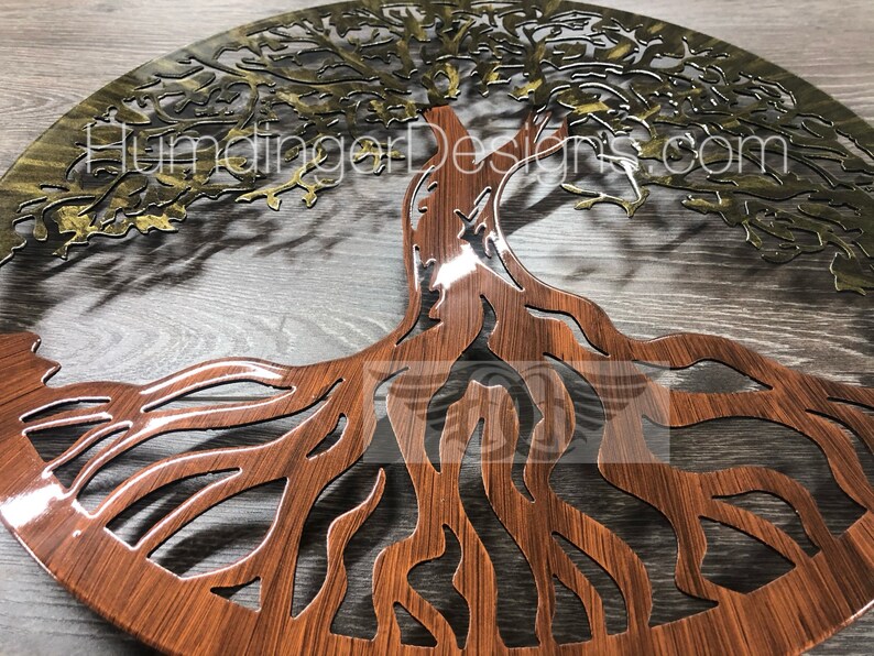 May include: A circular metal wall art piece depicting a tree of life with intricate branches and roots. The tree is cut out of the metal, revealing a wood-grain pattern underneath. The top half of the tree is painted gold, while the bottom half is painted brown.