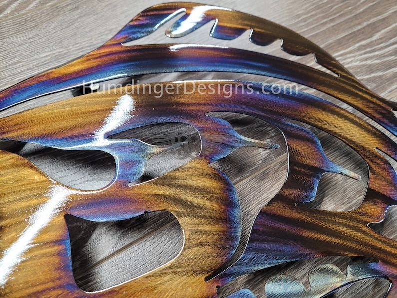 May include: A metal wall art piece in the shape of a butterfly with a blue, purple, and orange iridescent finish. The piece is cut out and has a detailed design.