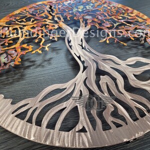 K&ouml;nnte beinhalten: Eine Wanddekoration aus Metall in Form eines Lebensbaums mit einer Kupfer- und Silber-Oberfl&auml;che. Der Baum hat ein detailliertes Design mit filigranen &Auml;sten und Wurzeln. Der Hintergrund ist eine dunkle Holzoberfl&auml;che.