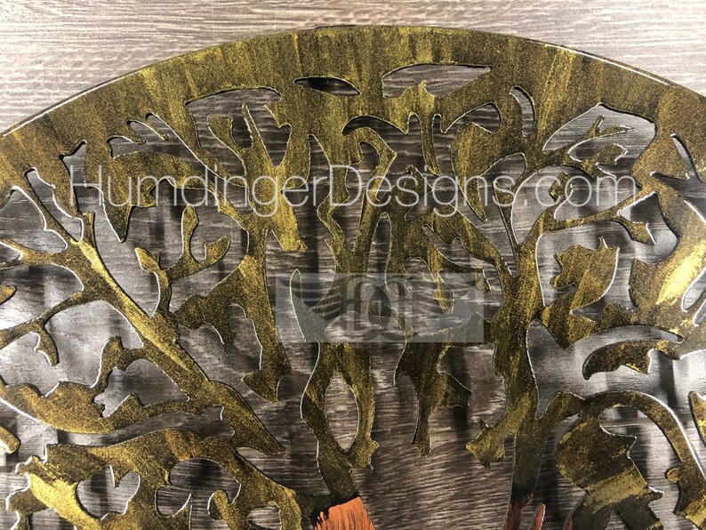 May include: A gold metal tree wall art with a cutout design. The tree is painted with a gold metallic paint and has a distressed finish.