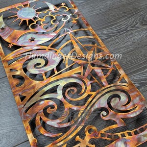 May include: A metal wall art piece with a nautical theme. The design features a crescent moon, stars, clouds, waves, and a compass rose. The metal is a copper color with a brushed finish.
