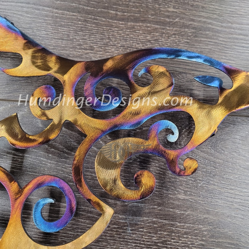 May include: A metal wall art piece with a swirling, abstract design. The metal has been heat treated to create a rainbow of colors, including blue, purple, gold, and orange.