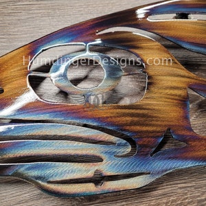 May include: A metal wall art piece in the shape of a fish with a blue, purple, and brown iridescent finish. The fish has a cut-out design and the text "HumdingerDesigns.com" is visible on the surface.