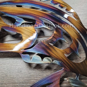 May include: A metal butterfly wall art with a cut-out design. The butterfly is painted with a rainbow iridescent finish, with shades of blue, purple, orange, and gold.