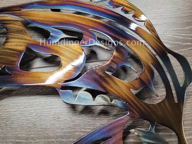 May include: A metal butterfly wall art with a cut-out design. The butterfly is painted with a rainbow iridescent finish, with shades of blue, purple, orange, and gold.