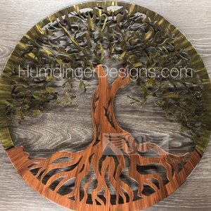 May include: A circular metal wall art piece depicting a tree of life with intricate branches and roots. The top half of the tree is painted gold, while the bottom half is painted a reddish-brown color. The text "HumdingerDesigns.com" is visible at the top of the artwork.
