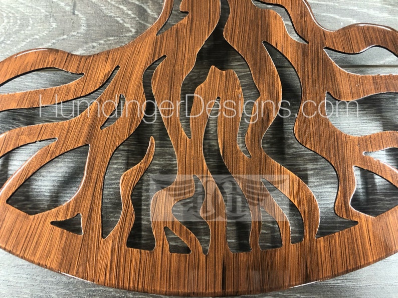 May include: A wooden wall decor in the shape of a tree with intricate cutouts of branches and roots. The wood has a brown stain and a glossy finish. The text "HumangerDesigns.com" is visible on the decor.