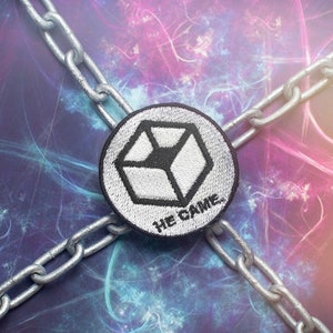 May include: A silver chain links across a colorful, abstract background. A black and white embroidered patch with a geometric design and the text "HE CAME." is centered in the image.