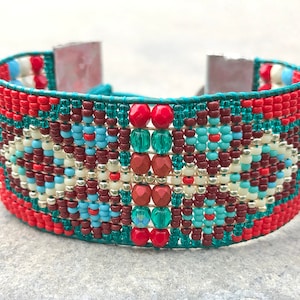 May include: A beaded bracelet featuring a geometric design in shades of red, teal, white, and brown. The bracelet is crafted with small seed beads and has a leather fastening.