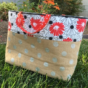 May include: A large tote bag with a white and black floral print on the top half and a brown burlap fabric with white polka dots on the bottom half. The bag has red and white polka dot straps.