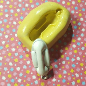 May include: A yellow silicone mould for making a small, white, vintage-style telephone. The mould is on a pink background with a pattern of white, yellow and blue stars.