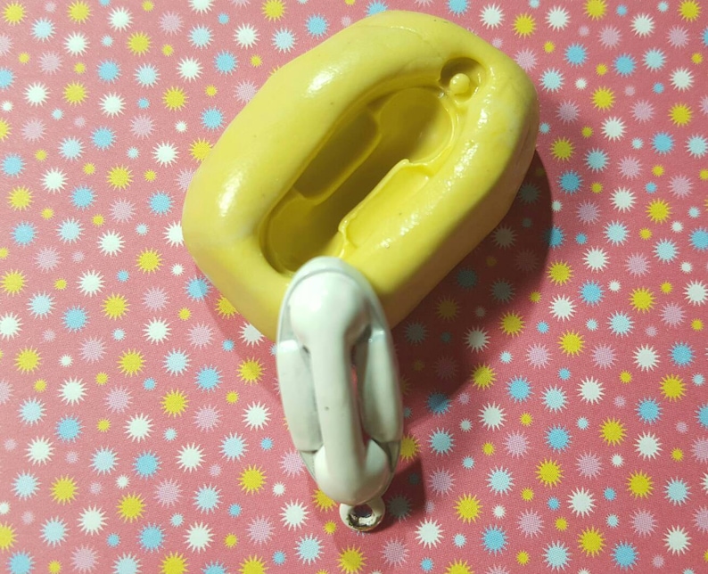 May include: A yellow silicone mould for making a small, white, vintage-style telephone. The mould is on a pink background with a pattern of white, yellow and blue stars.