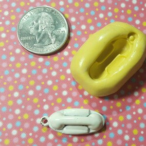 May include: A yellow silicone mould for making a small white rotary phone charm. The mould is shaped like a phone with a dial and a handset. A 25 pence coin is included for size reference.