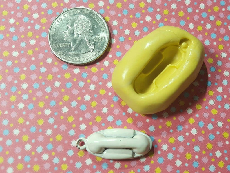 May include: A yellow silicone mould for making a small white rotary phone charm. The mould is shaped like a phone with a dial and a handset. A 25 pence coin is included for size reference.