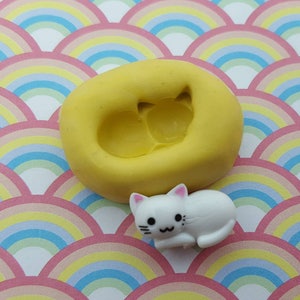 May include: Yellow silicone mold for making a small cat figurine. The mold has a detailed design of a cat lying down.