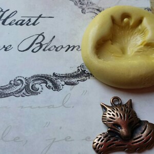 May include: A silicone mold for making a fox charm, with a bronze-colored fox charm next to it.