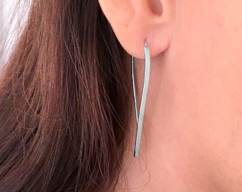 May include: Silver dangle earrings with a thin, curved design. The earrings are long and slender, and they hang from the earlobe.