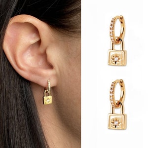 May include: Gold hoop earrings with a padlock charm featuring a small diamond. The padlock has a star design.