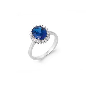 Könnte beinhalten: Ein silberner Ring mit einem großen ovalen blauen Edelstein, der von einem Heiligenschein aus kleineren weißen Edelsteinen umgeben ist.