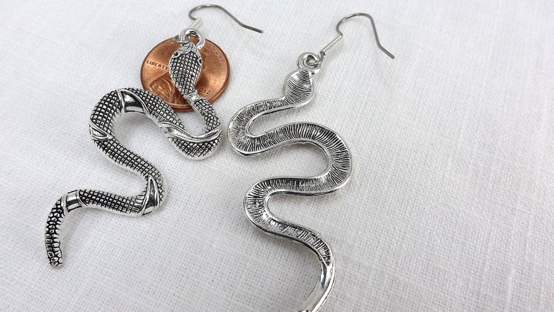 May include: A pair of silver snake earrings with a textured finish. The earrings are dangle style with a hook closure.