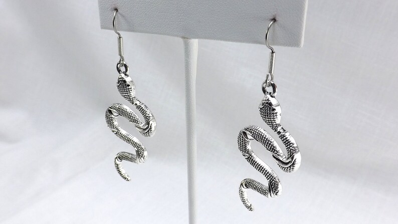 May include: Silver snake dangle earrings. The snake is coiled and has a textured surface.