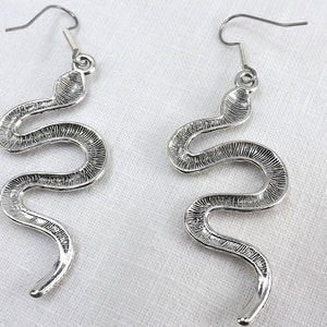 May include: A pair of silver snake dangle earrings. The earrings are made of metal and feature a detailed snake design.