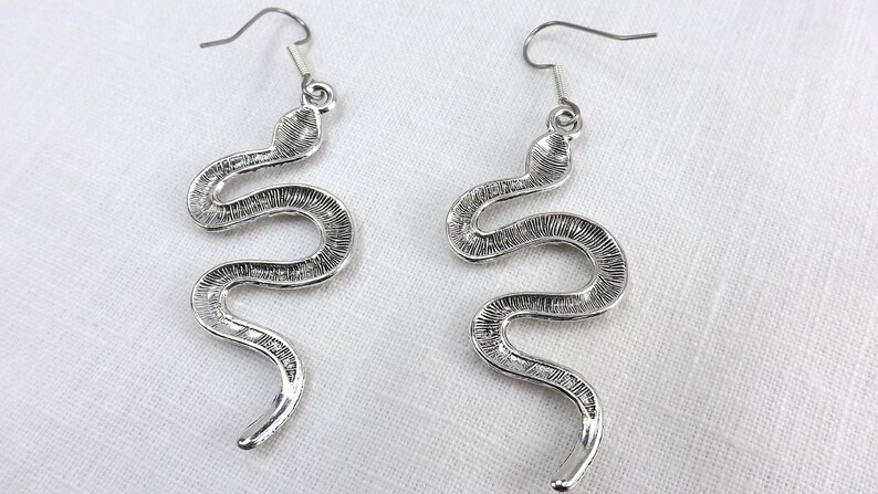 May include: A pair of silver snake dangle earrings. The earrings are made of metal and feature a detailed snake design.