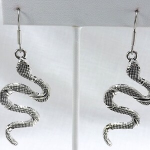 May include: A pair of silver snake dangle earrings. The snakes are coiled and have a textured surface.