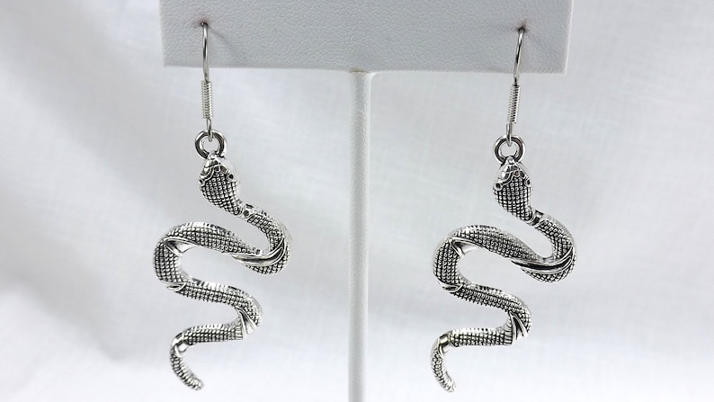 May include: A pair of silver snake dangle earrings. The snakes are coiled and have a textured surface.