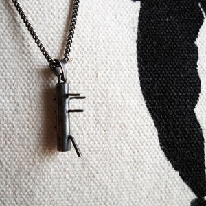 Puede incluir: Un collar de cadena de plata con un colgante de plata con forma de figura estilizada con múltiples brazos. El colgante está colgado sobre un fondo de tela blanca.