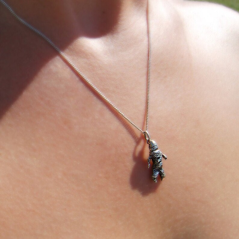 May include: A silver necklace with a small, detailed astronaut pendant. The astronaut is silver and has intricate detailing. The chain is delicate and hangs against a person's skin.