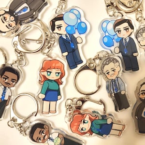 May include: A set of ten colorful cartoon character keychains. The characters are all wearing different outfits and have different expressions. Some of the characters are holding balloons. The keychains are made of clear acrylic and have silver metal key rings.