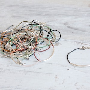 May include: A pile of colorful leather bracelets with silver clasps. Some bracelets are layered on top of each other. A single black leather bracelet with a silver bar is on the right side of the image.