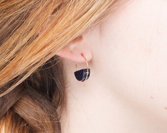May include: A pair of gold hoop earrings with a dark blue, speckled, semi-circular accent.