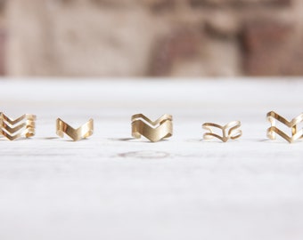 Puede incluir: Conjunto de cuatro anillos de metal dorado con diseño de chevron. Los anillos están dispuestos en una fila sobre una superficie blanca.