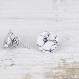 Könnte beinhalten: Ein Paar weiße und schwarze marmorierte Ohrstecker mit silbernen Stiften.
