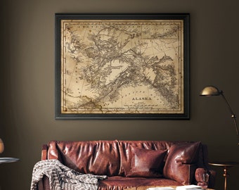 May include: A vintage map of Alaska in a black frame hangs above a brown leather sofa with a throw blanket. A lamp and side table are on the right side of the sofa. The map is titled "ALASKA" and shows the coastline and major rivers.