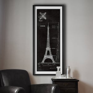 Pode incluir: Um desenho arquitetônico em preto e branco da Torre Eiffel em Paris, França. O desenho está emoldurado e pendurado em uma parede em uma sala com uma poltrona de couro preto e uma mesa auxiliar de madeira.
