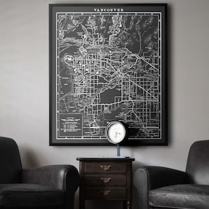 Può includere: Una mappa in bianco e nero di Vancouver, Canada, incorniciata in nero, è appesa a un muro sopra un tavolino nero con un orologio in cima. Due poltrone in pelle nera sono posizionate su entrambi i lati del tavolo.