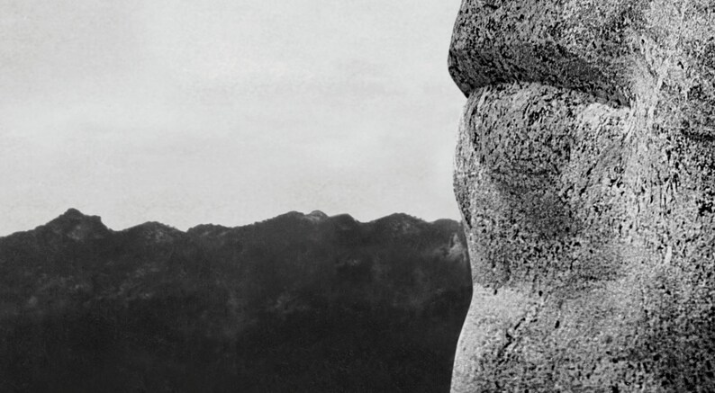 May include: A close-up of a large, grey rock formation with a rough, textured surface. The rock appears to be part of a larger structure, possibly a mountain or a statue. The background is a blurred, grey sky.