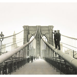 Puede incluir: Fotograf&iacute;a en blanco y negro del puente de Brooklyn. Dos hombres con trajes y sombreros est&aacute;n de pie sobre un soporte del puente, se&ntilde;alando. Los peatones caminan por la plataforma del puente. Se ven las torres y los cables del puente.