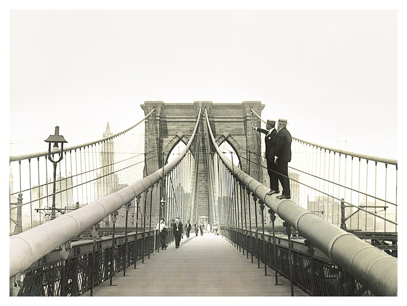 Puede incluir: Fotograf&iacute;a en blanco y negro del puente de Brooklyn. Dos hombres con trajes y sombreros est&aacute;n de pie sobre un soporte del puente, se&ntilde;alando. Los peatones caminan por la plataforma del puente. Se ven las torres y los cables del puente.
