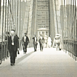 Puede incluir: Fotograf&iacute;a en blanco y negro de personas caminando por un puente. El puente tiene cables verticales y una pasarela. Varias personas caminan en la misma direcci&oacute;n.