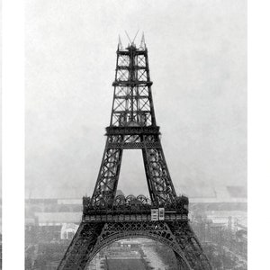 May include: Black and white photograph of the Eiffel Tower under construction. The iconic wrought-iron lattice tower is partially built, with visible scaffolding and construction elements. The image captures the tower's intricate design and the surrounding cityscape.