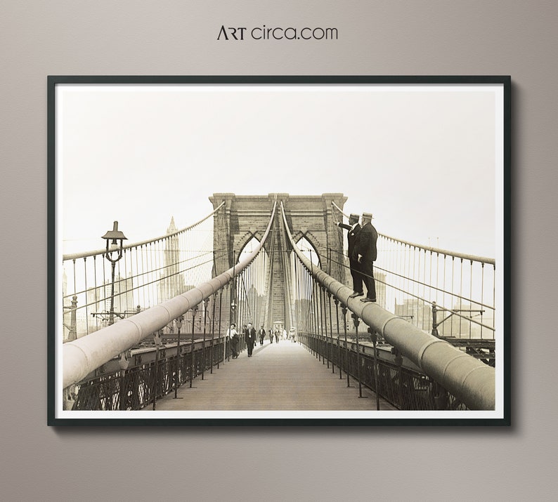 Puede incluir: Impresi&oacute;n enmarcada en tonos sepia del puente de Brooklyn. Dos hombres con trajes est&aacute;n de pie sobre una tuber&iacute;a, se&ntilde;alando. Los peatones caminan por la pasarela de madera. La imagen es de Art Circa.