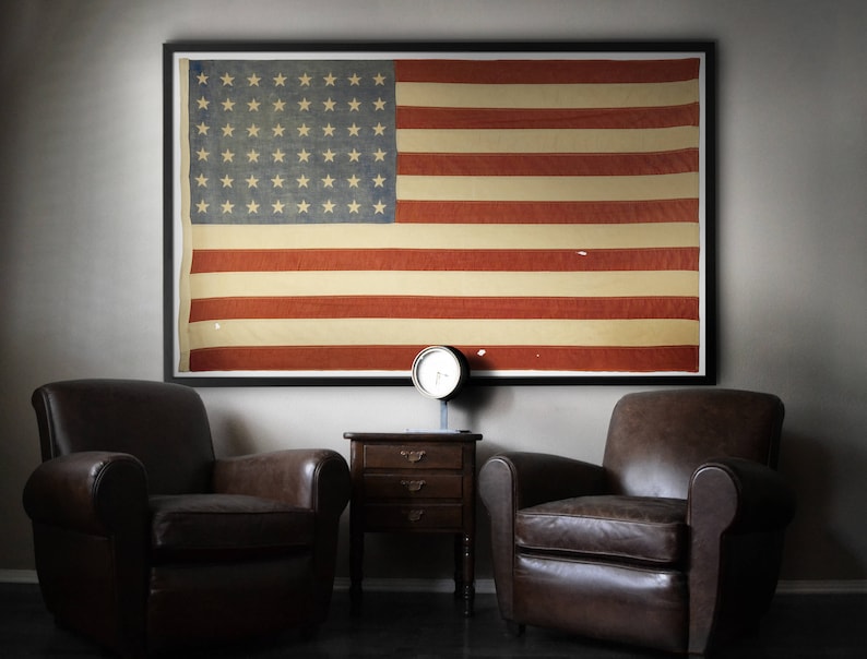 Framed print of vintage American flag on wall with leather club chairs. Come be inspired by 4th of July Tablescapes, Patriotic Decor & USA Finds: Happy Birthday, America in case you're in the mood for American flag and red, white, and blue festive finds.